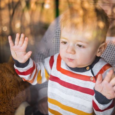 A toddler presses hands on a window, looking outside thoughtfully.