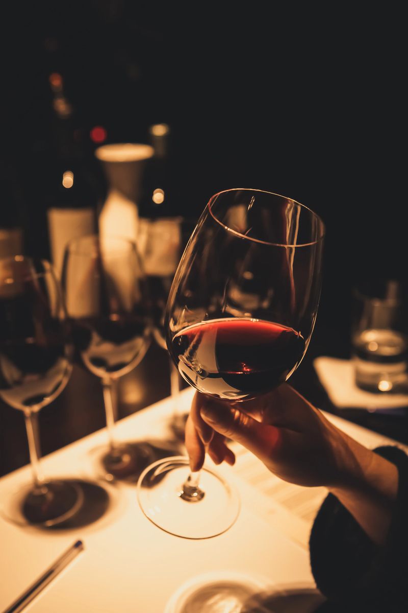 Woman holding and swirling a glass of red wine during a wine tasting event in a dark room with other glasses of wine in the background.