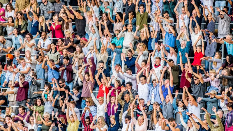 Large crowd of people doing a Mexican wave during a sports event on a stadium.
