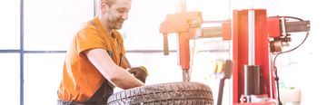 Worker fitting a rugged off-road tire with golden bolts on a black and orange rim.