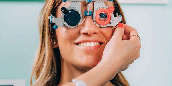 Woman smiling while getting an eye exam with a phoropter.