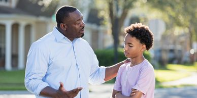 Father gently talks to his son outdoors in a caring manner.