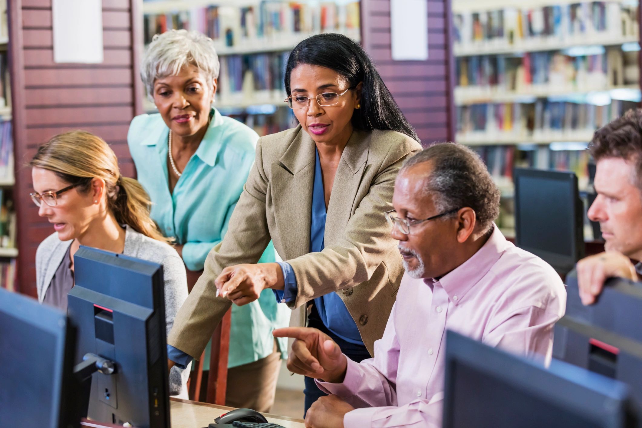 Group of adults collaborating on computers in a library setting.
