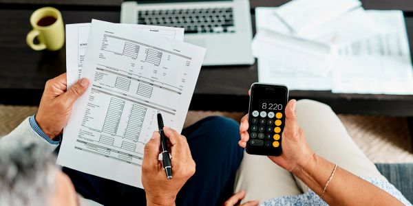 Two people calculating finances using documents and a phone calculator.