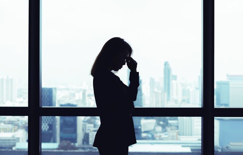 Depressed asian business woman standing at windows with city view background