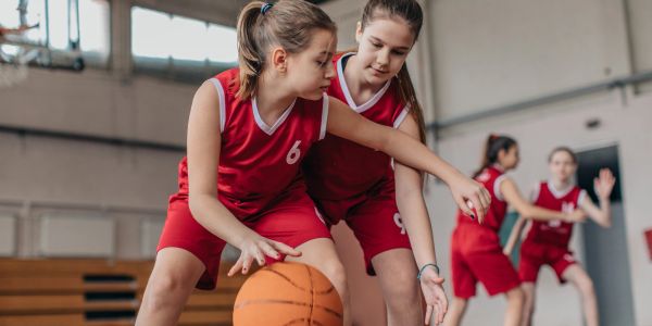 Two young girls playing basketball indoors.
