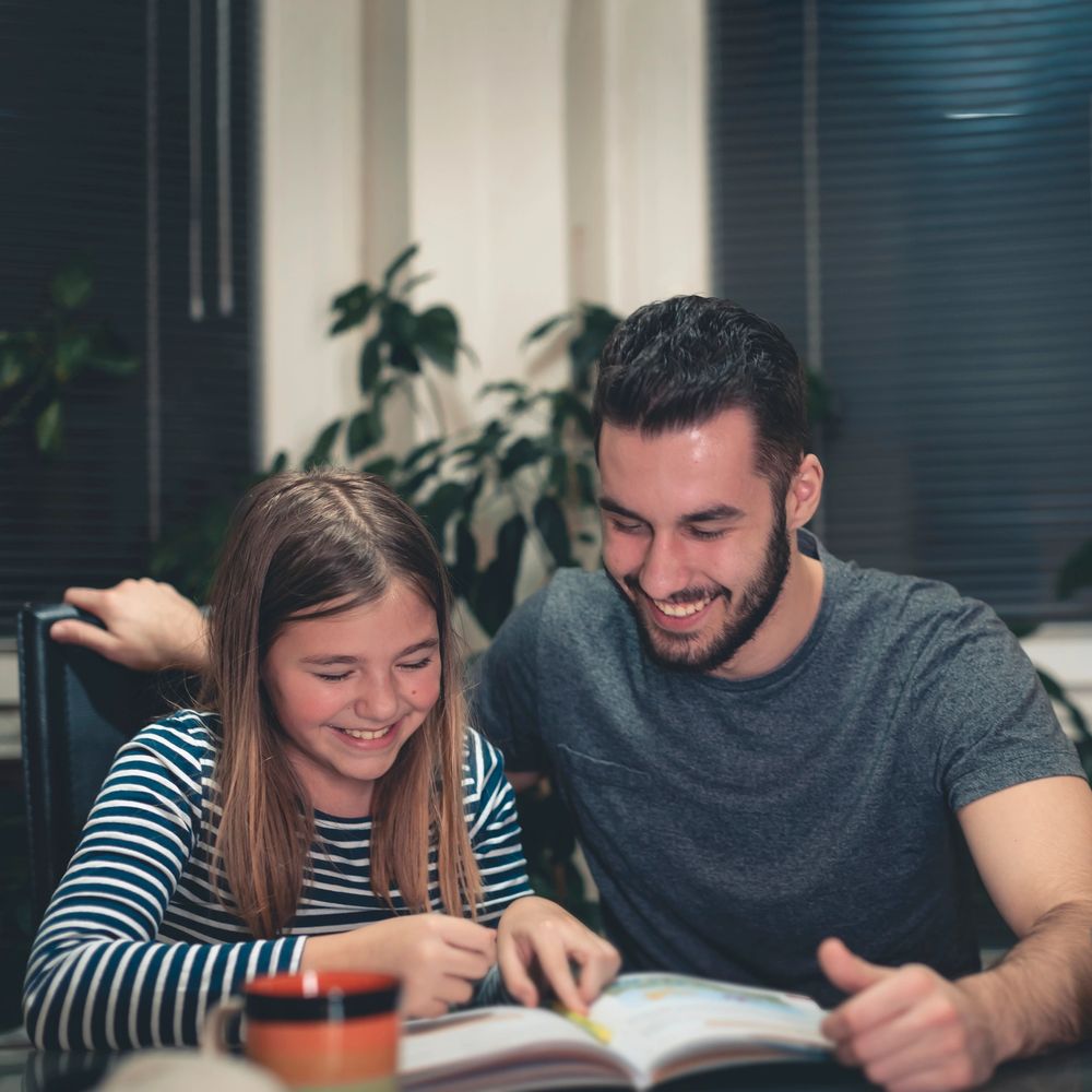 A man and a girl happily reading a book together at a table.