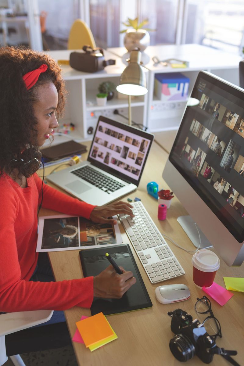 Side view of young mixed-race female graphic designer using graphic tablet at desk in a modern office