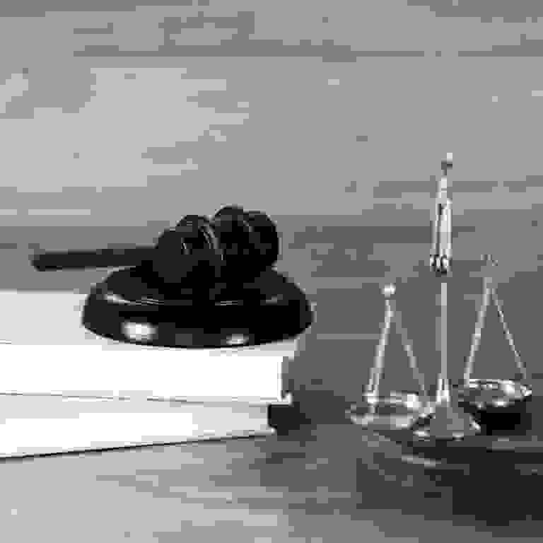 Judge's gavel on books with golden scales of justice on wooden table.