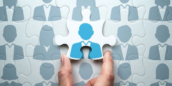 Hand placing a puzzle piece with a blue businessperson icon among gray icons.