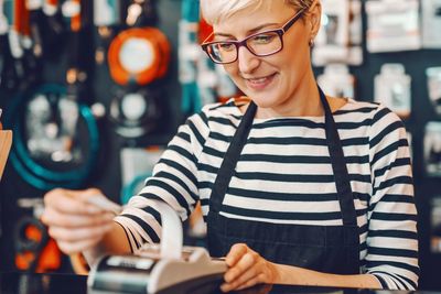 Smiling barista using a receipt printer in a cozy coffee shop.