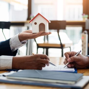 Two people signing a document with a small house model.