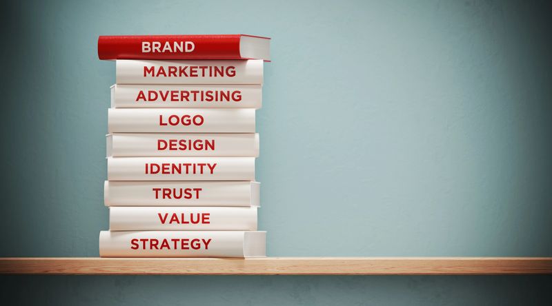 Books of advertising, marketing  and branding are sitting on top of each other. The books have unique texts on their spines related to brand subject.