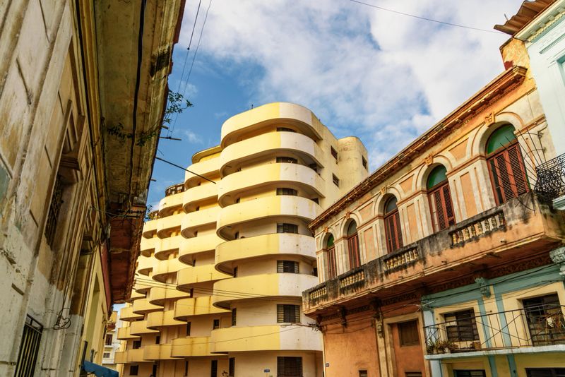 street with yellow art deco apartment building beside old houses in old havana