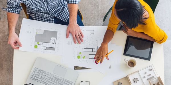 Two people reviewing architectural floor plans at a workspace.