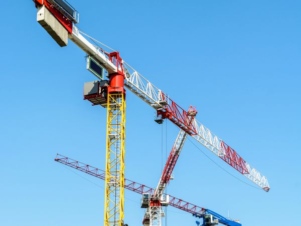 Three colorful construction cranes against a clear blue sky.