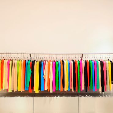 Colorful sweaters neatly hung on a rack against a plain wall.