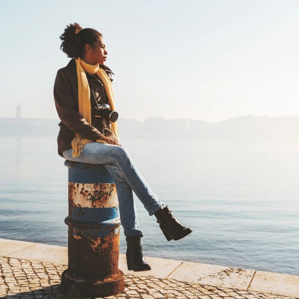 Woman sitting by water with camera and scarf.