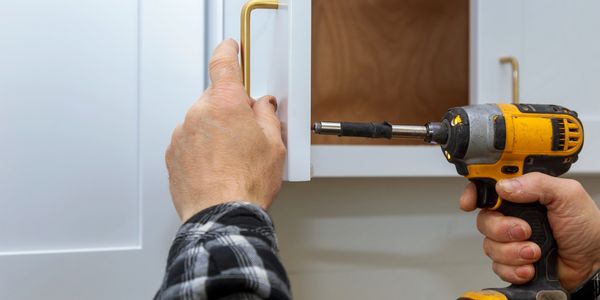 Person installs cabinet handle using a power drill.