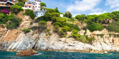 Coastal cliffside with greenery and houses under a blue sky.