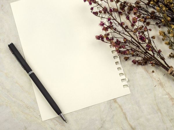 Blank notepad with a pen and dried flowers on a marble surface.