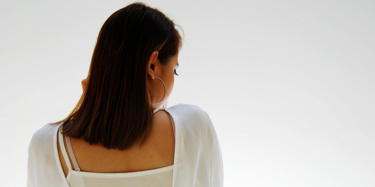Woman with shoulder-length hair wearing hoop earrings and a white top, seen from behind.