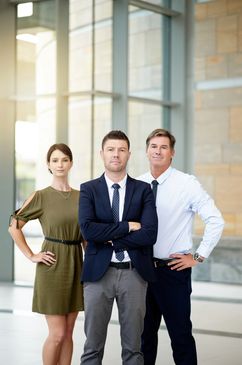 Three confident professionals posing in an office environment.