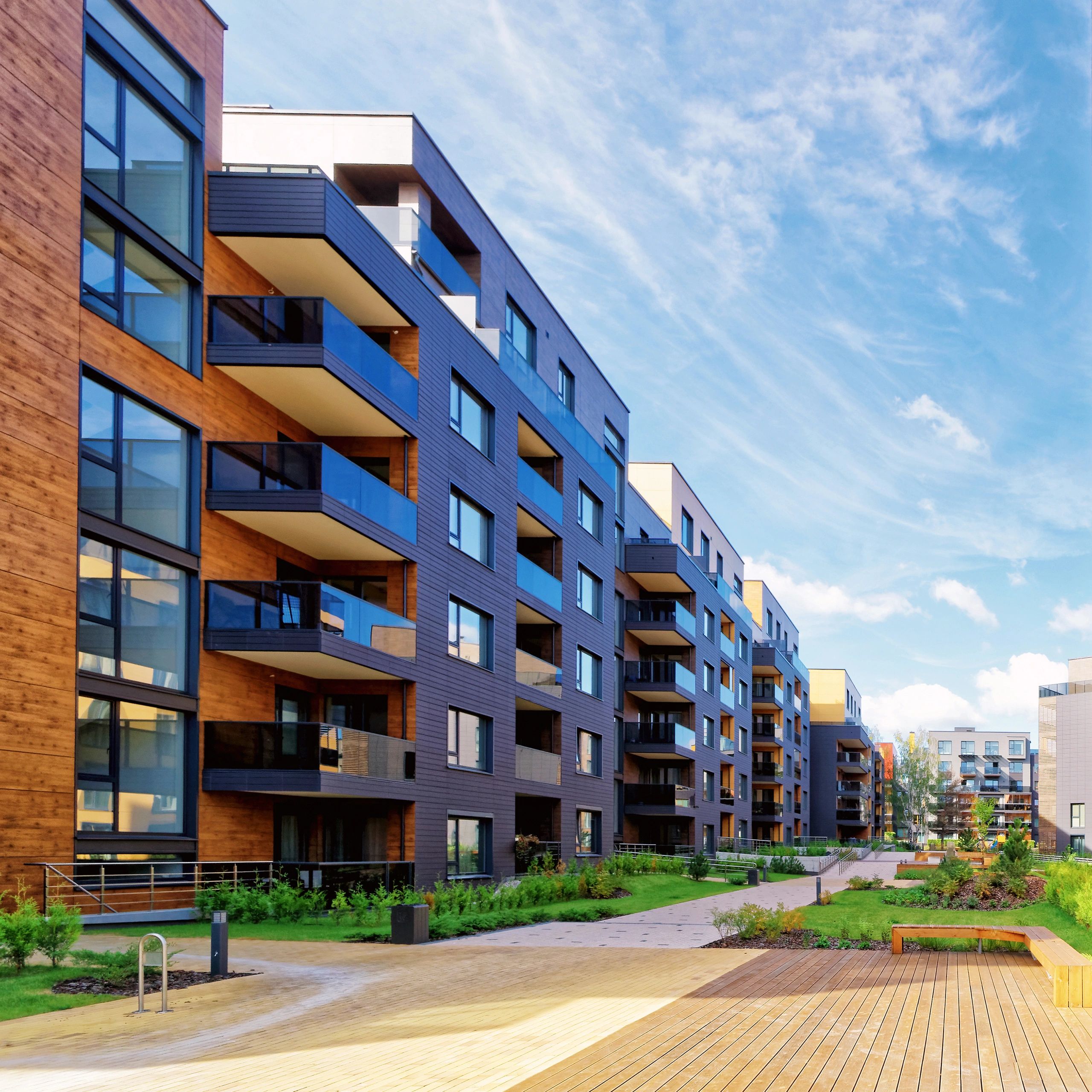 Modern apartment buildings with balconies and a landscaped courtyard under a blue sky.