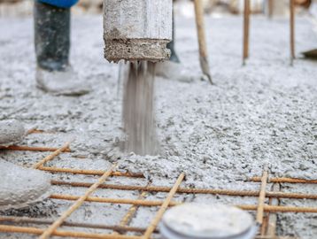 Fresh concrete being poured over a steel reinforcement grid at a construction site.