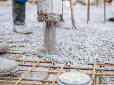 Wet concrete being poured over steel reinforcement bars at a construction site.