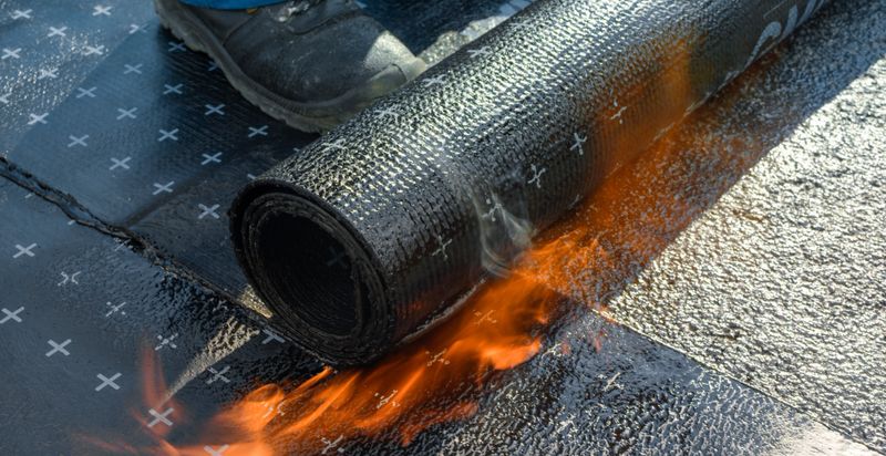 Construction worker heating and melting bitumen rolls.