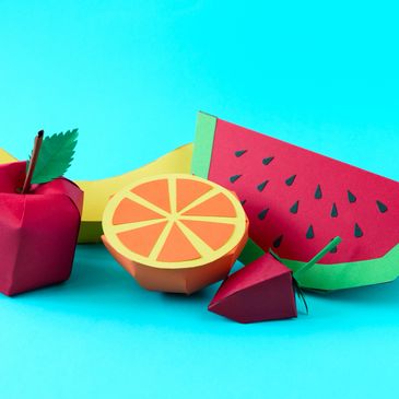 Colorful paper craft fruits arranged on a blue background.