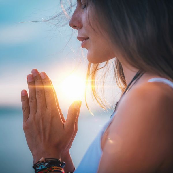 Woman praying during sunset with hands together.