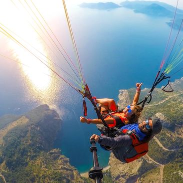 Two people paragliding over a scenic coastline with clear blue waters.