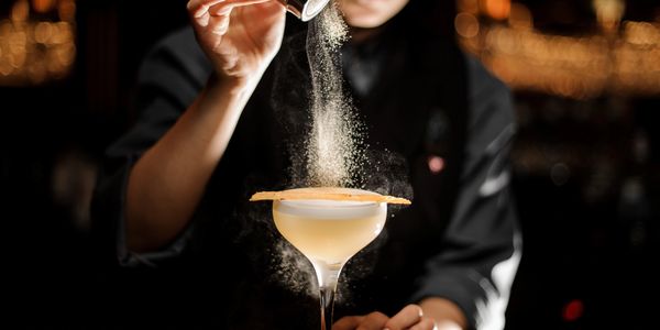 Bartender dusts a cocktail with powder in a dimly lit bar.