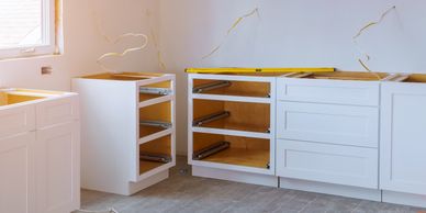 White kitchen cabinets being installed in an unfinished kitchen space.