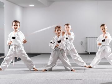 Four children practicing karate in white uniforms and black belts.