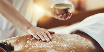 A relaxing salt scrub massage being applied on a person's back in a spa setting.