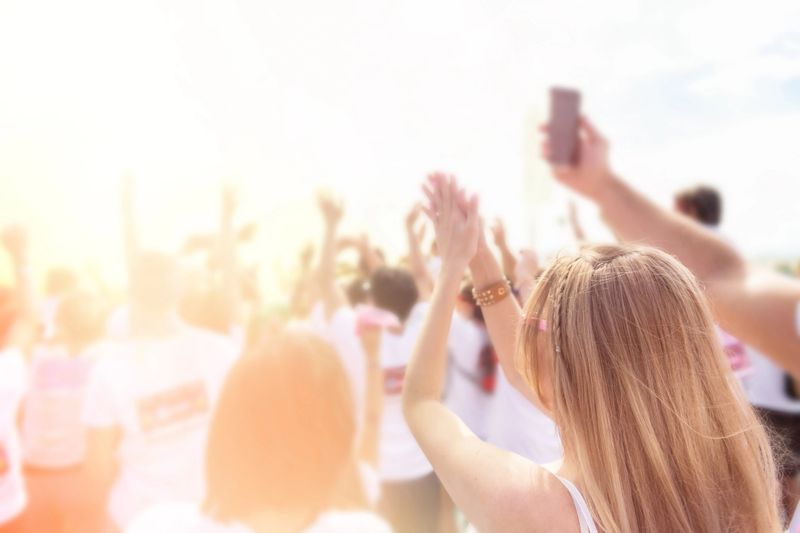 Young cheering woman fan at music festival standing with arms raised, clapping and applauding in the crowded music concert outdoors.