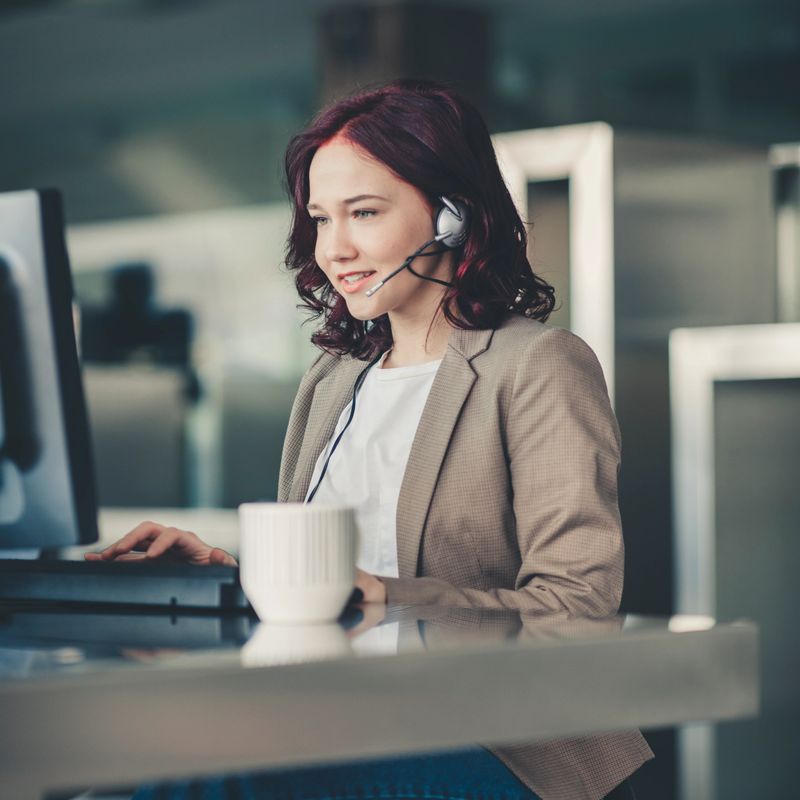 Beautiful young woman telephone operator with headset working on desktop computer  in  customer service call support helpline business center with teamworker in background