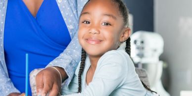 Smiling girl with braided hair baking with help from an adult.