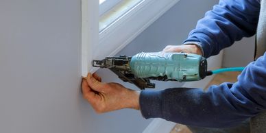 Person using a nail gun on a window frame.