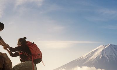 A person helping another climb a mountain with a snowy peak.