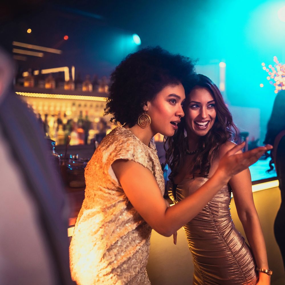Two women in elegant dresses enjoying a night out at a bar.