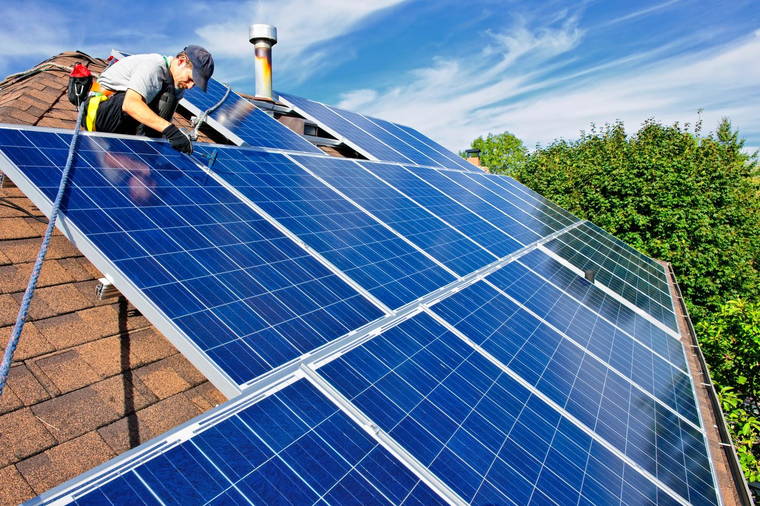 Worker installing solar panels on a rooftop under a clear sky.