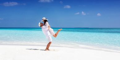 Couple joyfully embracing on a pristine white beach with clear turquoise water.