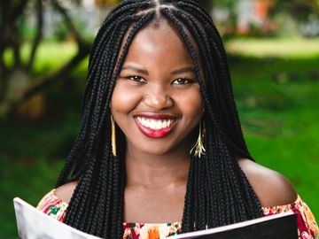 Smiling woman with braided hair holding a book outdoors.