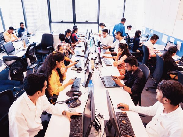 Busy office with many people working on computers and phones.