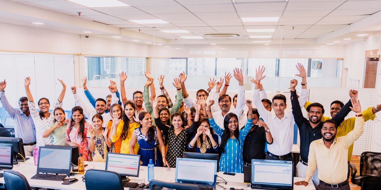 A diverse group of office employees celebrating with raised hands.