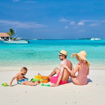 Family enjoying a sunny day at the beach with turquoise water and sand toys.